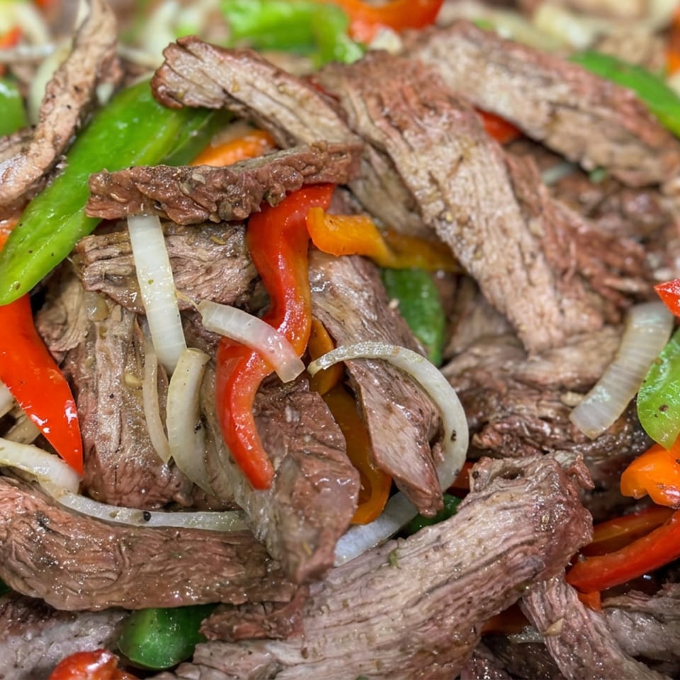 Sautéed beef strips with red and green bell peppers and onions in a skillet.